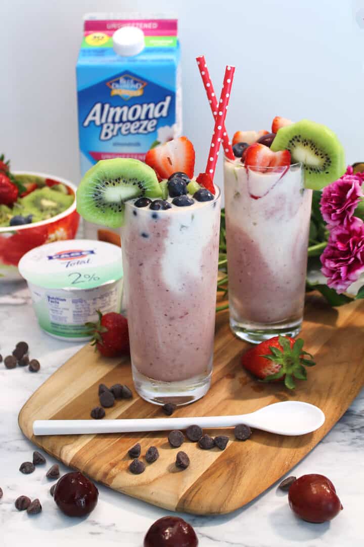 Two smoothies with chocolate chips around them and flowers in back.