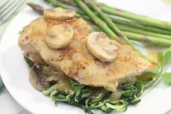 Chicken on top of zucchini noodles and drizzle with wine sauce and mushrooms on white plate