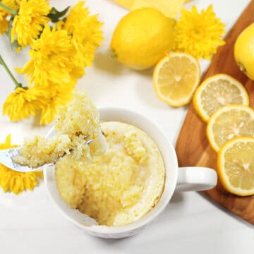 Bite of lemon cake in a mug on table with lemons.