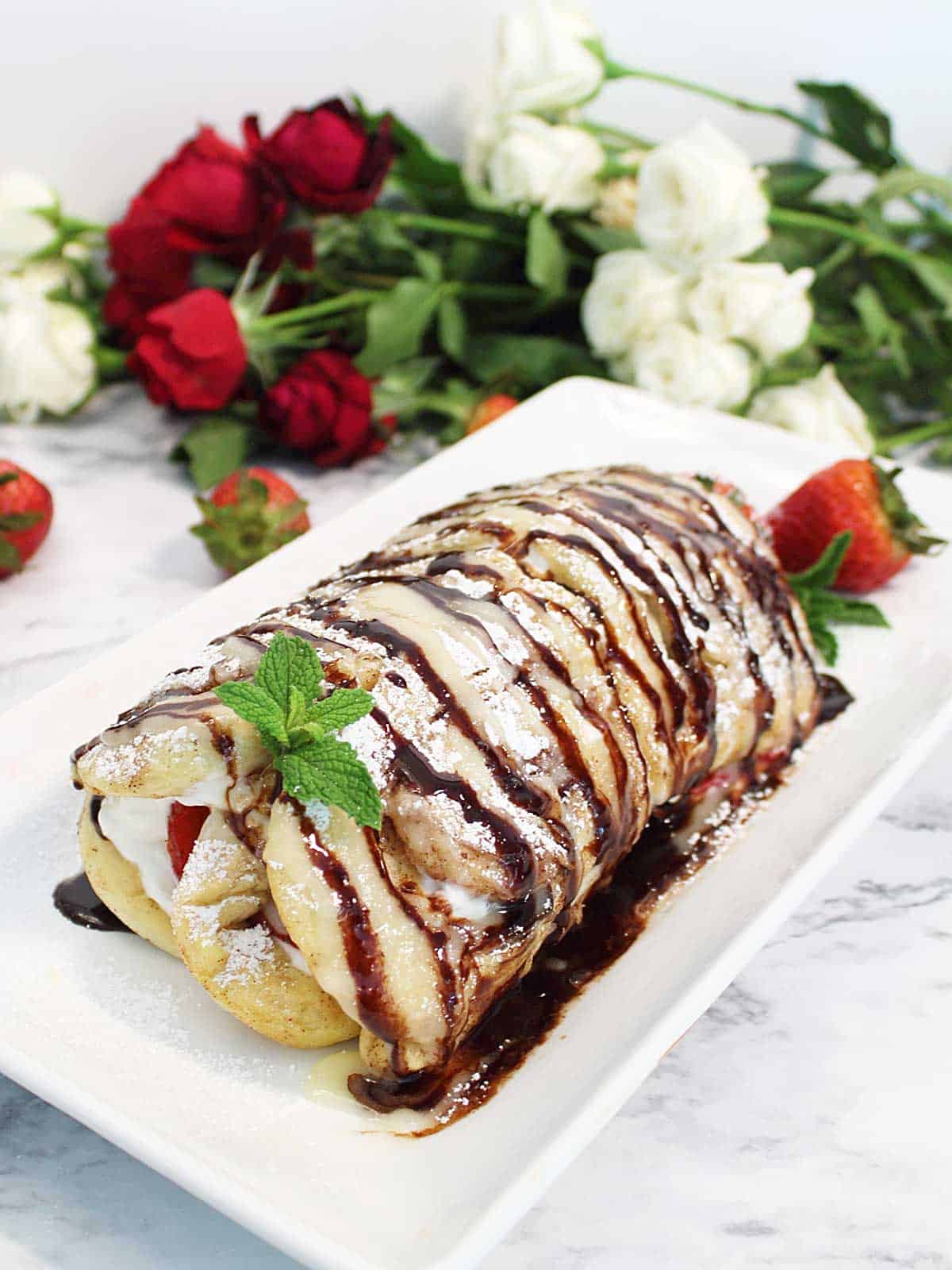 An easy brunch treat that starts with packaged cinnamon rolls. Bake and fill with sweetened Greek yogurt and sliced strawberries, roll up, then drizzle with icing and chocolate. Perfect for kids to make for mom on Mother's Day or just for a quick dessert for those unexpected guests. #sweetroll #easy #recipe #strawberry #Greekyogurt #MothersDay #brunch #dessert #cinnamonroll #breakfast #quick Strawberry Cinnamon Roll plated.