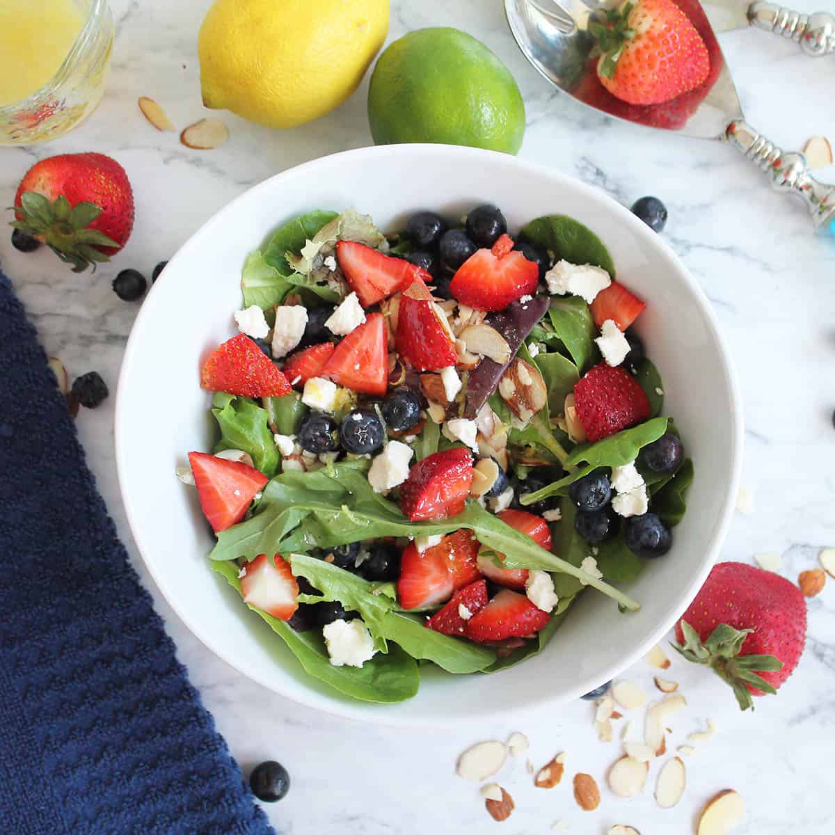 Overhead of Mixed Berry Salad in white bowl with fruit and nuts scattered around.