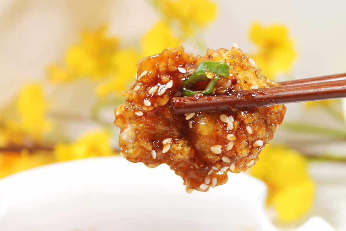 Closeup of chopsticks holding piece of chicken.