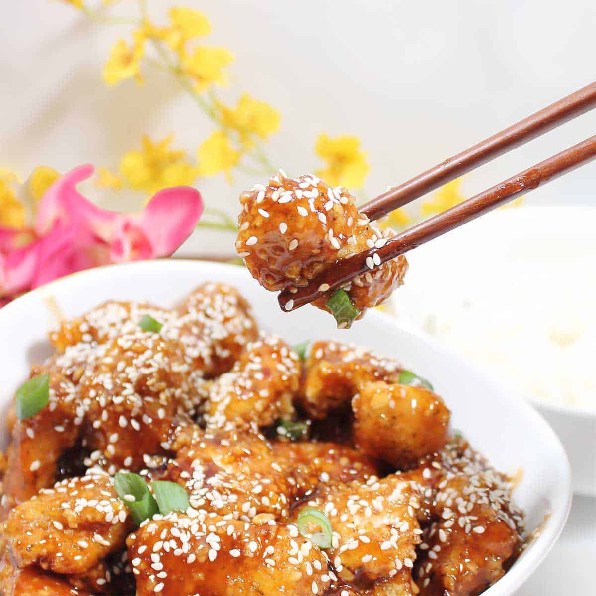 Holding piece of chicken with chopsticks over bowl.