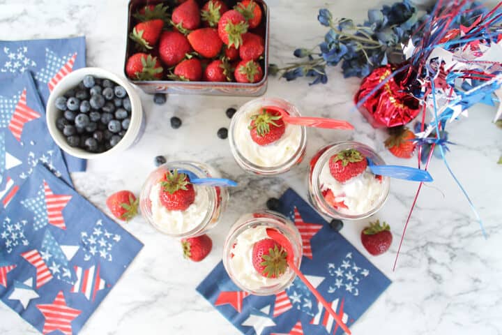 Overhead of 4 patriotic parfaits on marble table with berries.