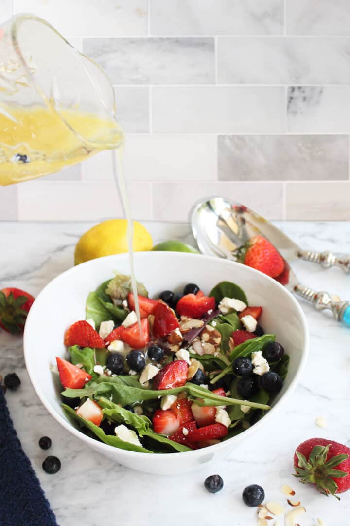 Pouring dressing over salad on marble table.