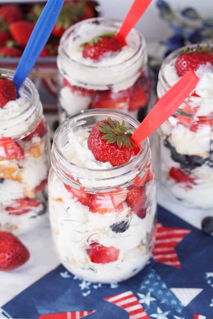 4 mason jar parfaits with red and blue spoons on white table.