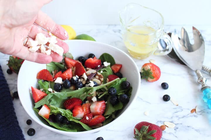 Sprinkling feta cheese on top of mixed greens and berries.