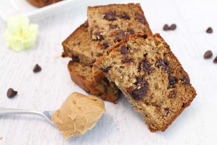 Slices of chocolate chip banana bread with spoonful of peanut butter on white table.