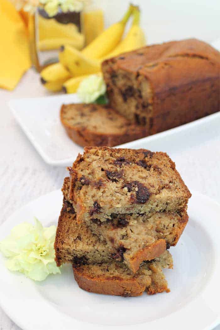 Stacked slices of banana bread with whole bread and bananas in background.