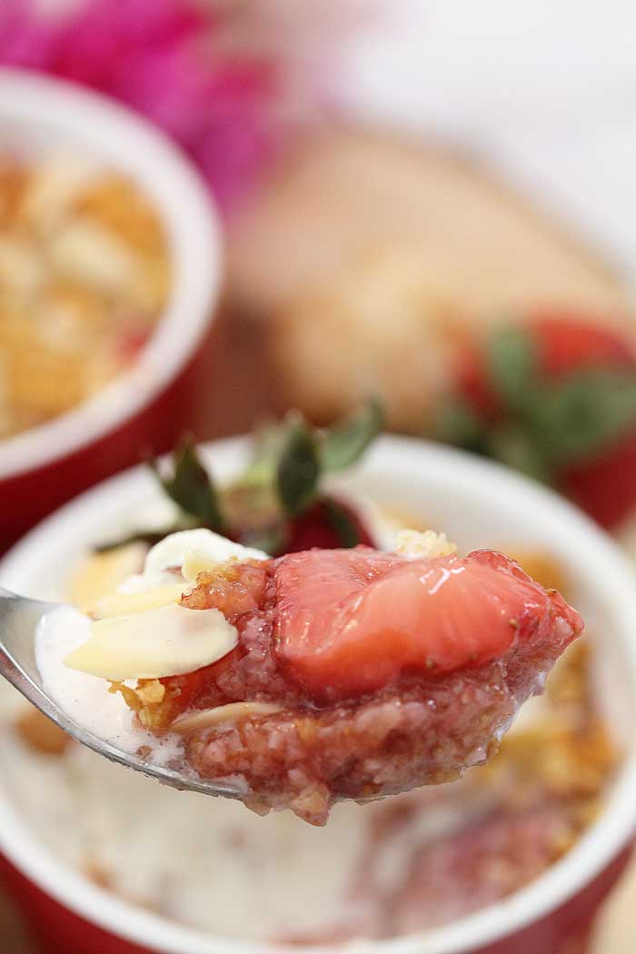 Closeup of bite with sliced strawberry and ice cream on spoon.