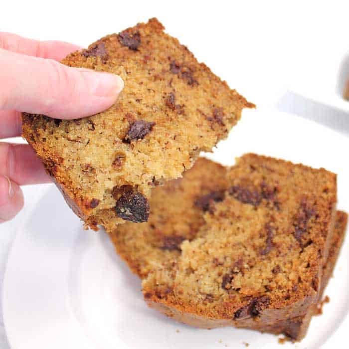 Grabbing a piece of banana bread off white plate.