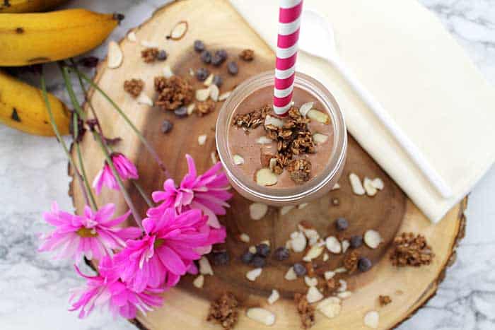 Finished smoothie in mason jar with granola and almonds on top sitting on wood.