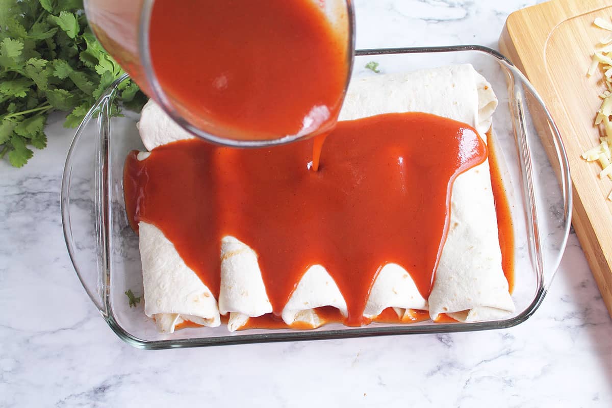 Pouring enchilada sauce over rolled enchiladas.