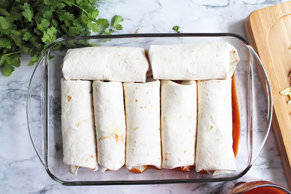 Enchiladas in baking dish on top of enchilada sauce.