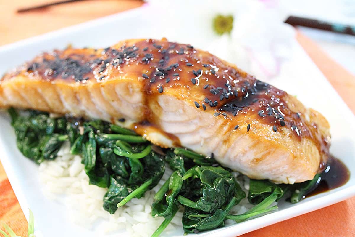 Closeup of plated Asian baked salmon over spinach on white plate.