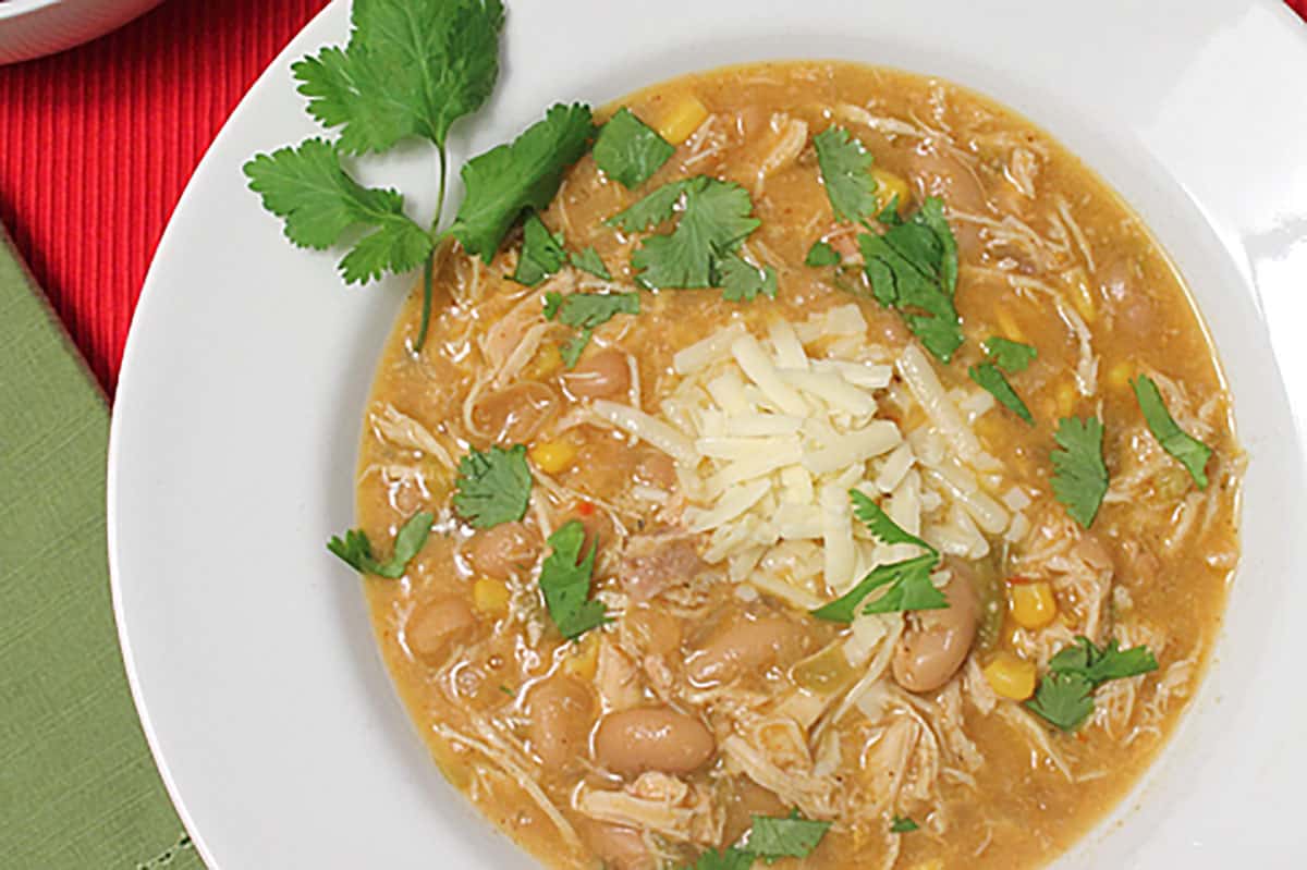 Chili serving in white bowl with cheese and cilantro garnish.