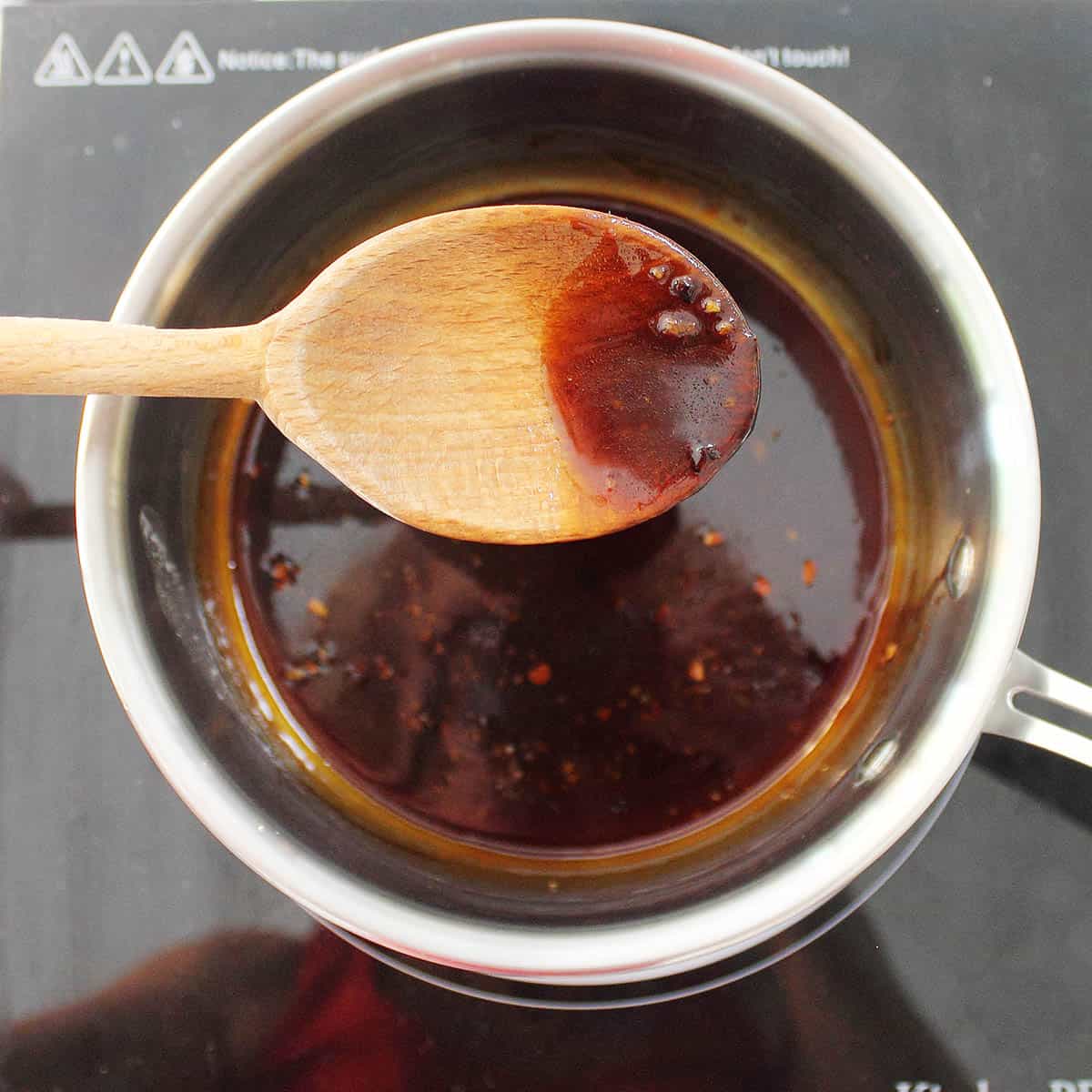 Closeup of thickened maple sauce on wooden spoon.