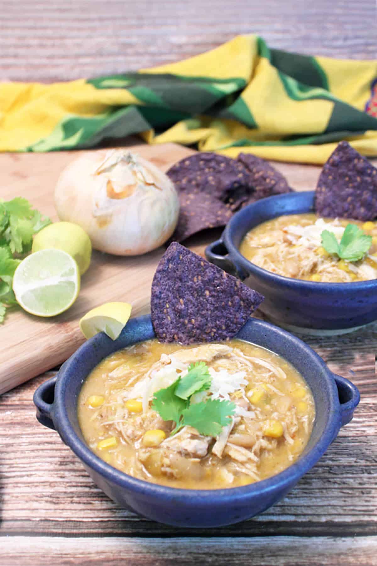 Two bowls of chili on wooden table with cutting board.