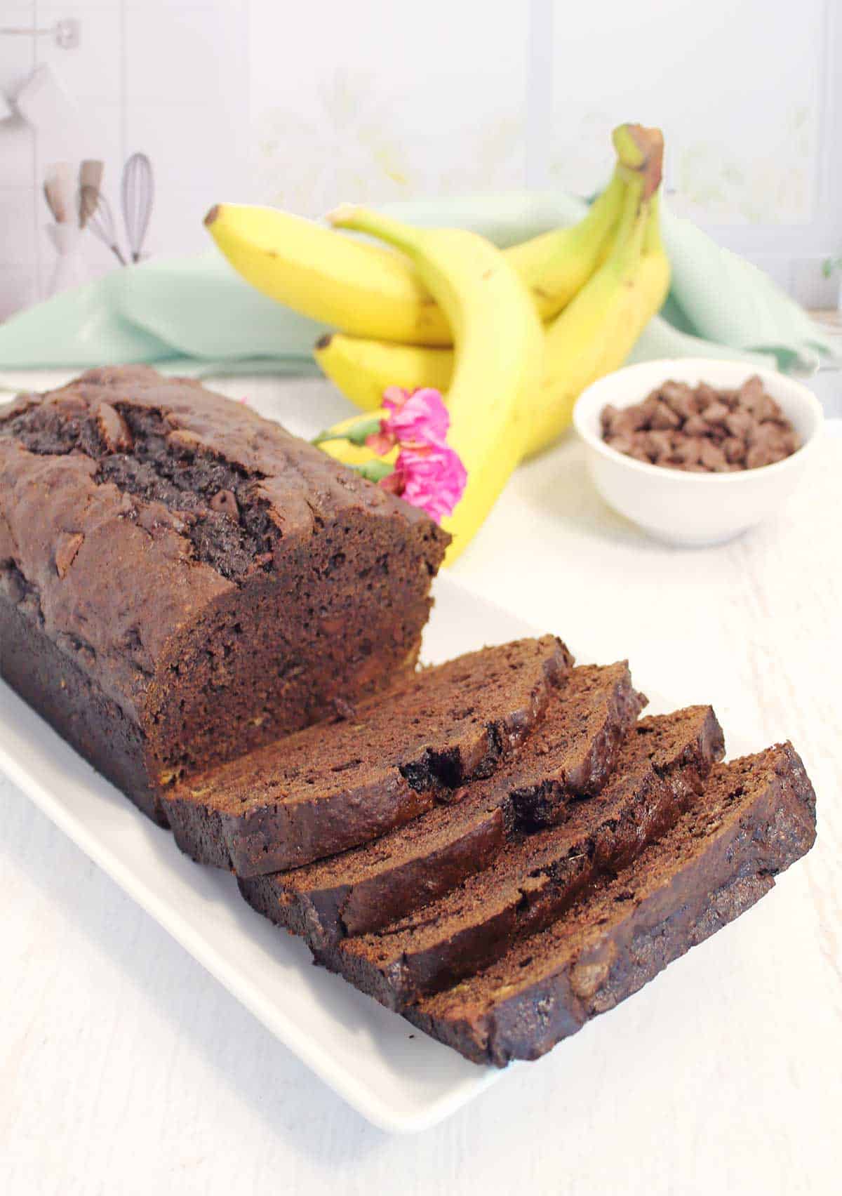 Sliced double chocolate banana bread with bananas on kitchen counter.
