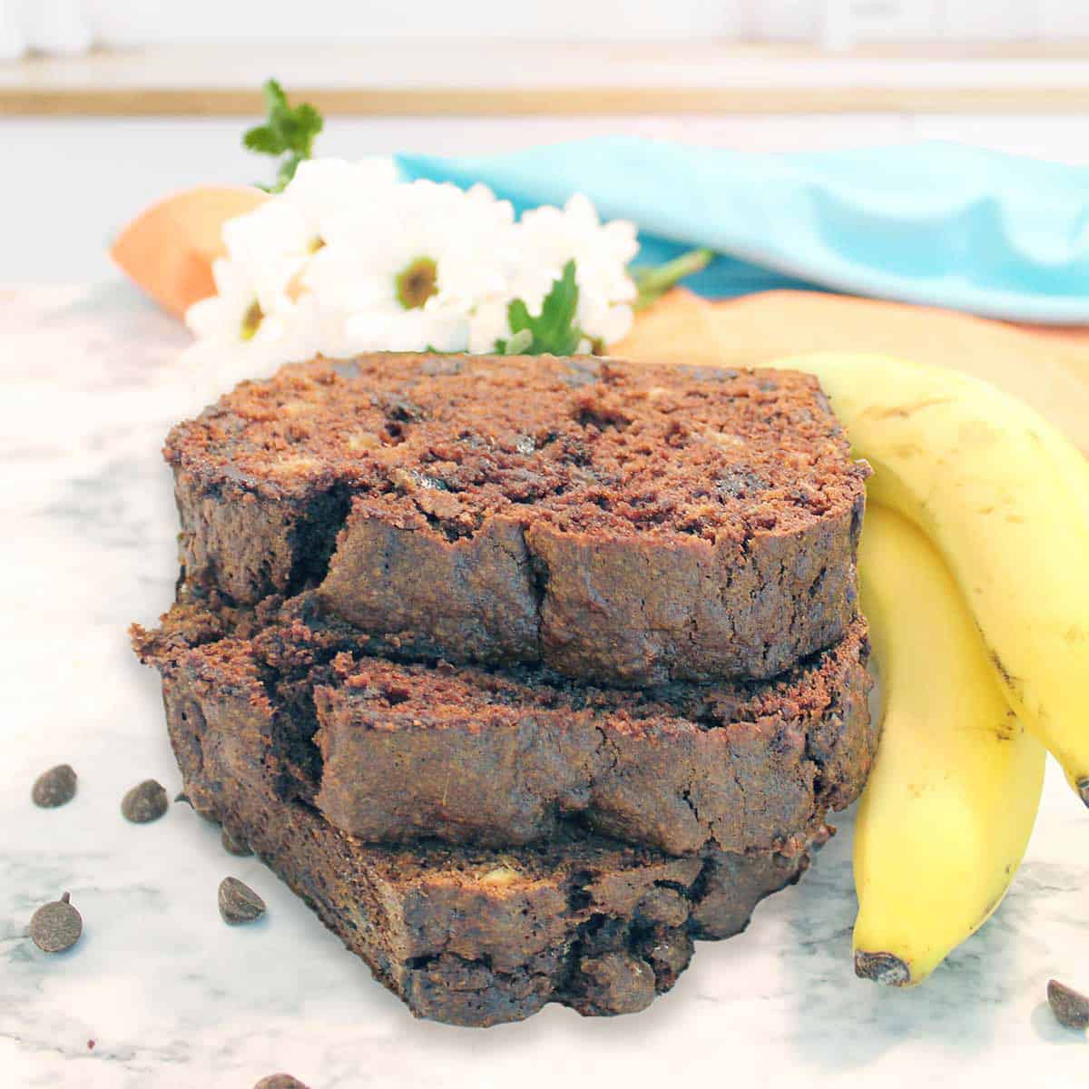 Closeup of stack of double chocolate banana bread slices with flowers and bananas.