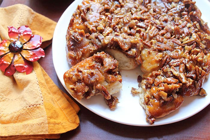 A plateful of warm maple pecan sticky buns with fall napkin and flower ring on the side.