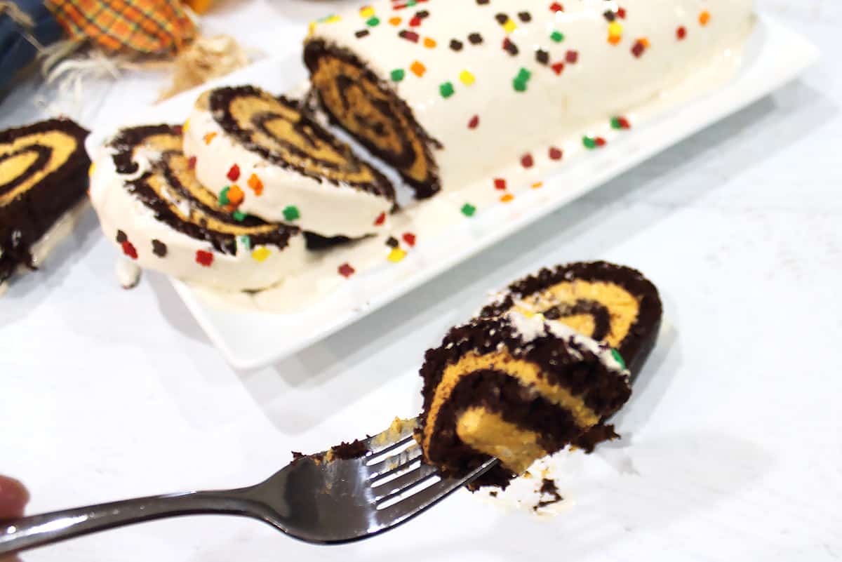 Bite of swiss role on fork over sprinkled cake.