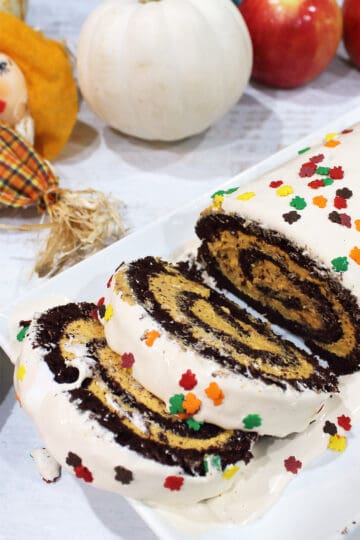 Chocolate Swiss Roll sliced showing pumpkin filling with pumpkins in back.