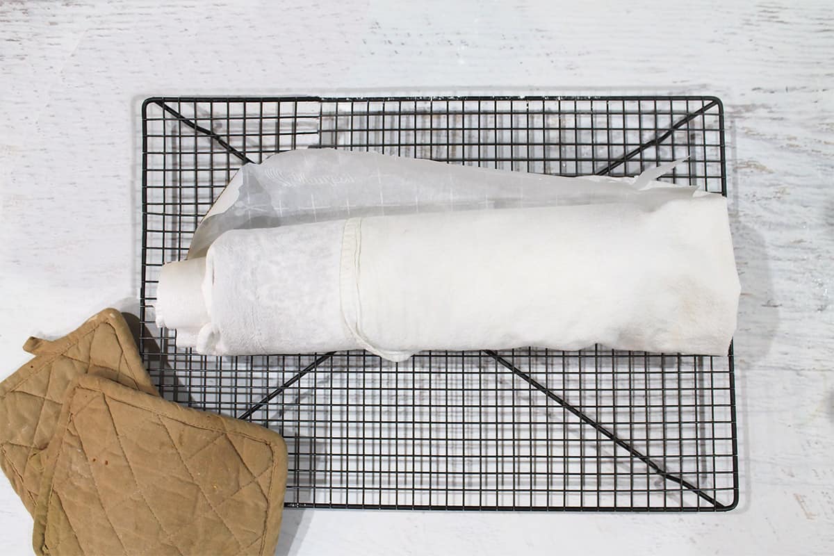 Cake rolled in towel on wire rack.