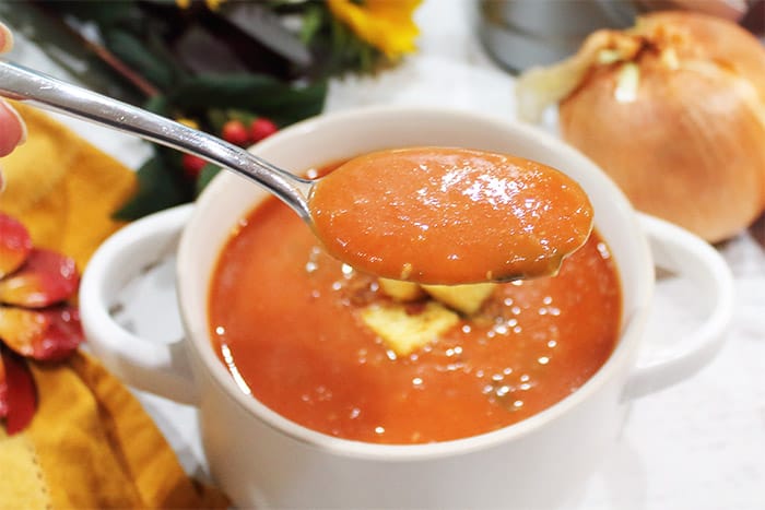 Spoonful of tomato basil soup in white bowl.