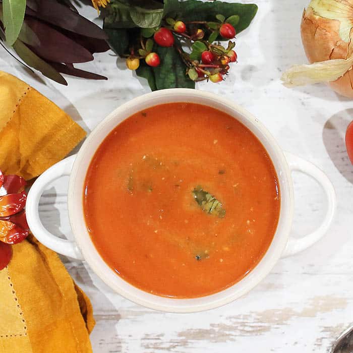 Overhead of Tomato Basil Soup in white bowl on white table.