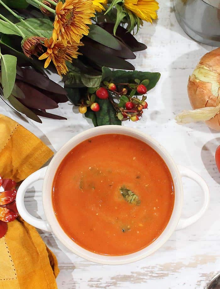 Blender Tomato Basil Soup in white bowl on white table with gold napkin.
