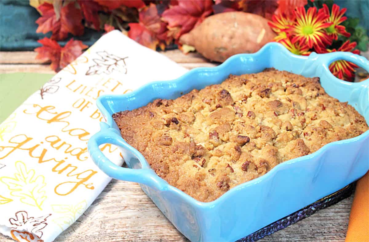 Sweet Potato Casserole in turquoise dish on wooden table with sweet potato and fall leaves in back.