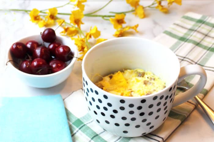 Cooked egg breakfast in white polka dot mug on green plaid towel.