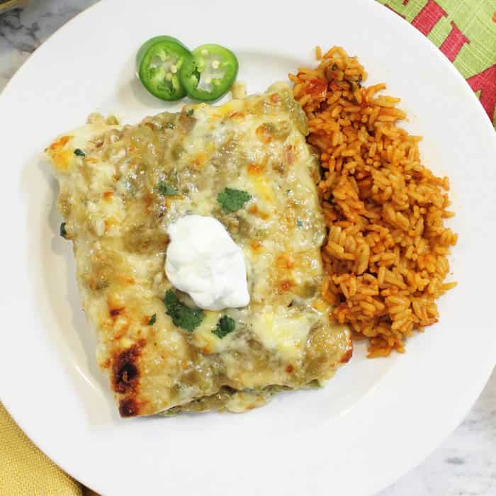 overhead of smothered green chile chicken burritos on white plate with spanish rice.