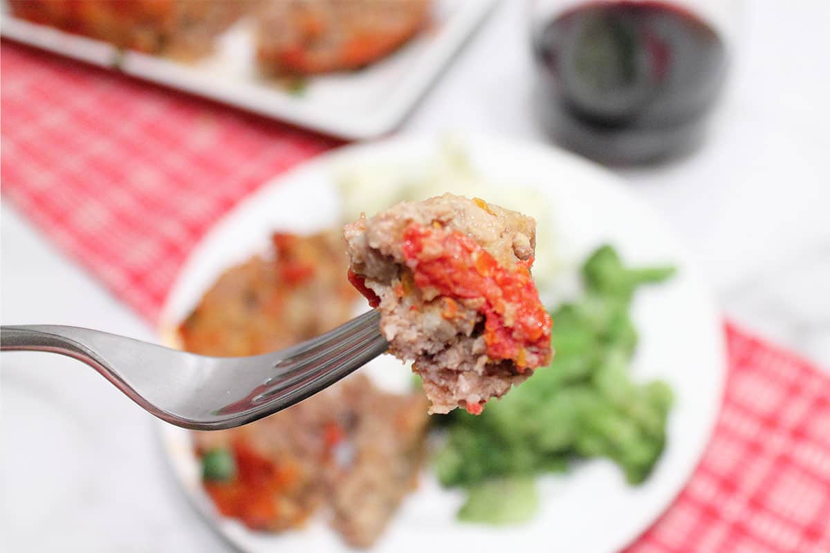 Bite of meatloaf on fork over dinner plate.