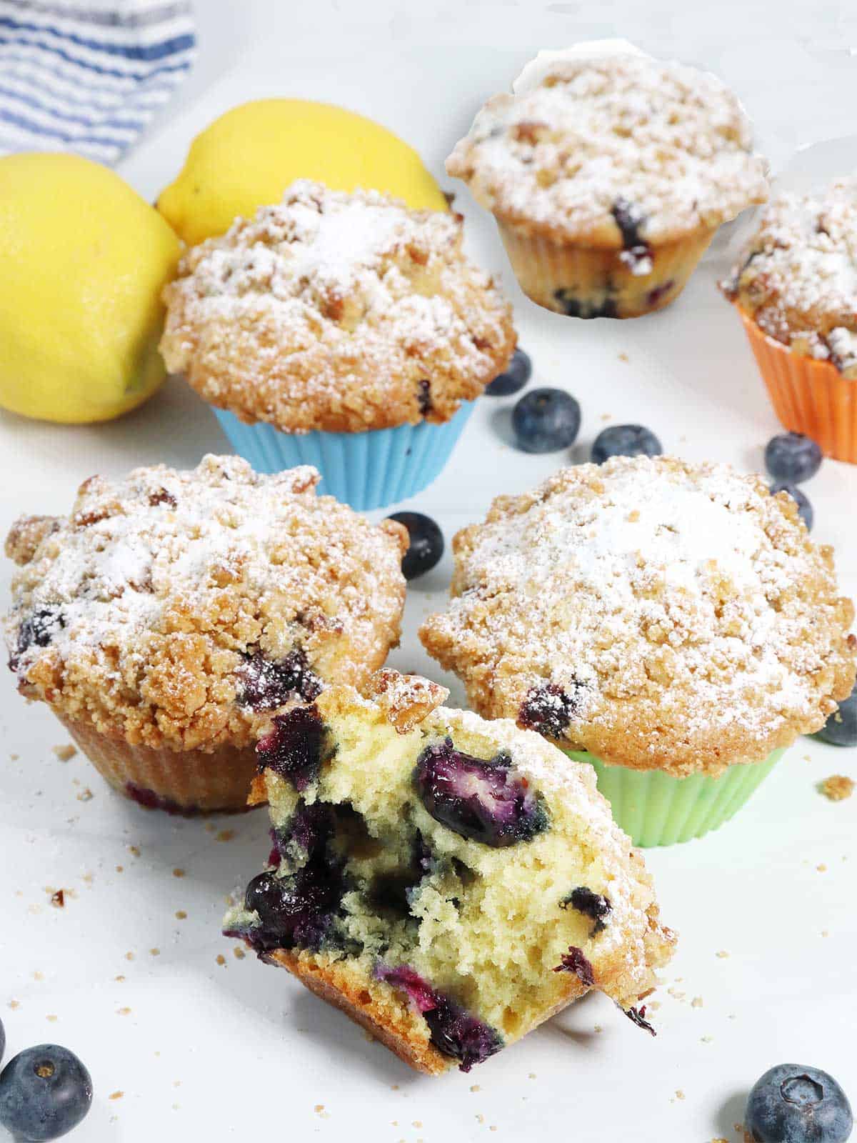 Blueberry and lemon muffins scattered on table with one halved in front.