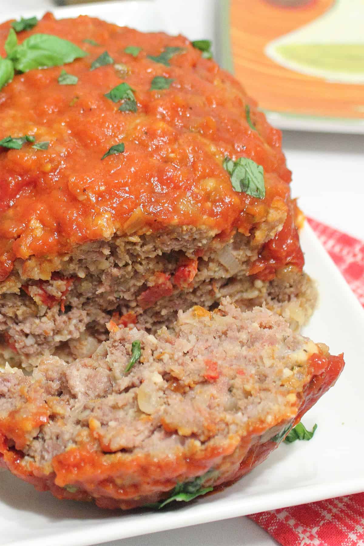 Meatloaf on white serving plate with one piece sliced.