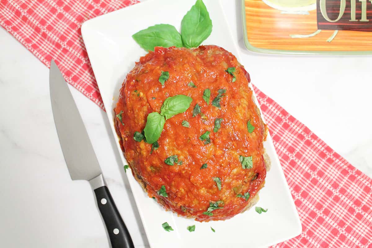 Overhead of meatload garnished with basil on white plate.