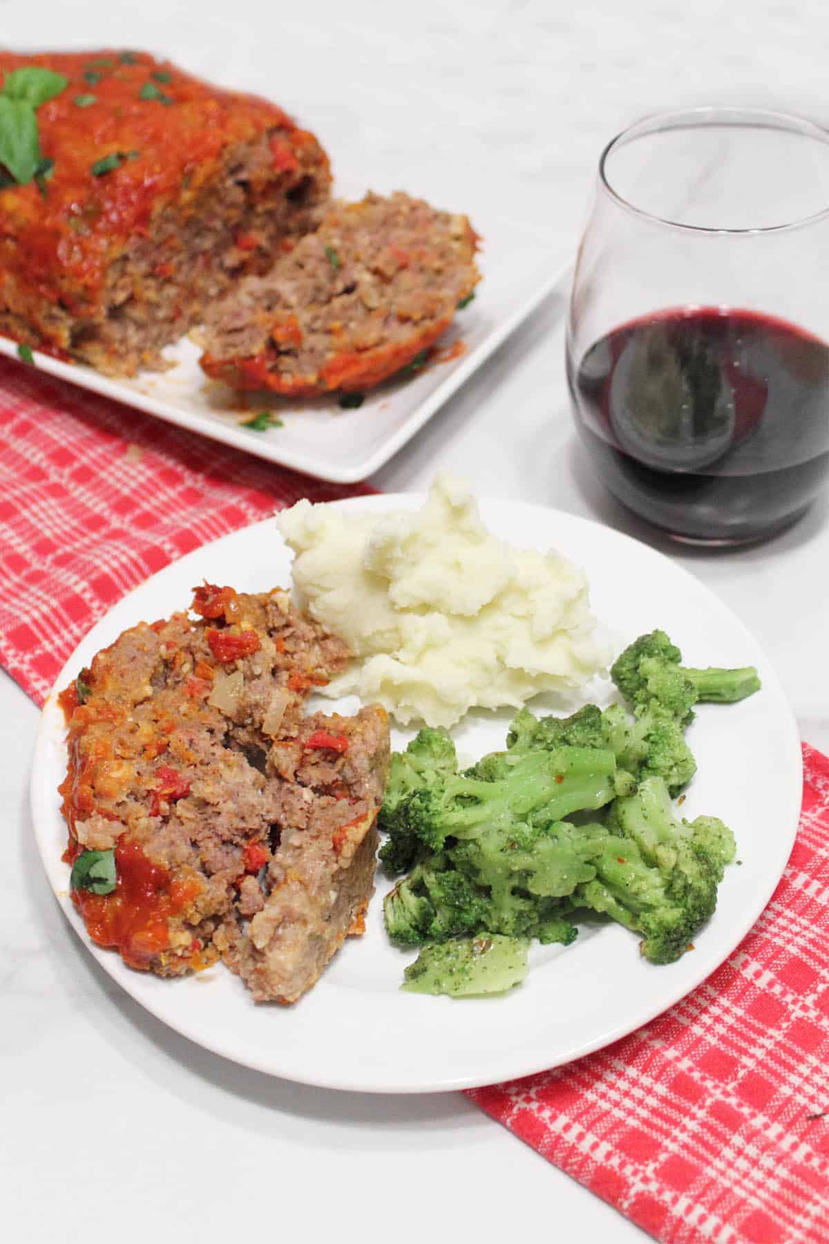 Plated dinner with meatloaf in background and glass on wine.