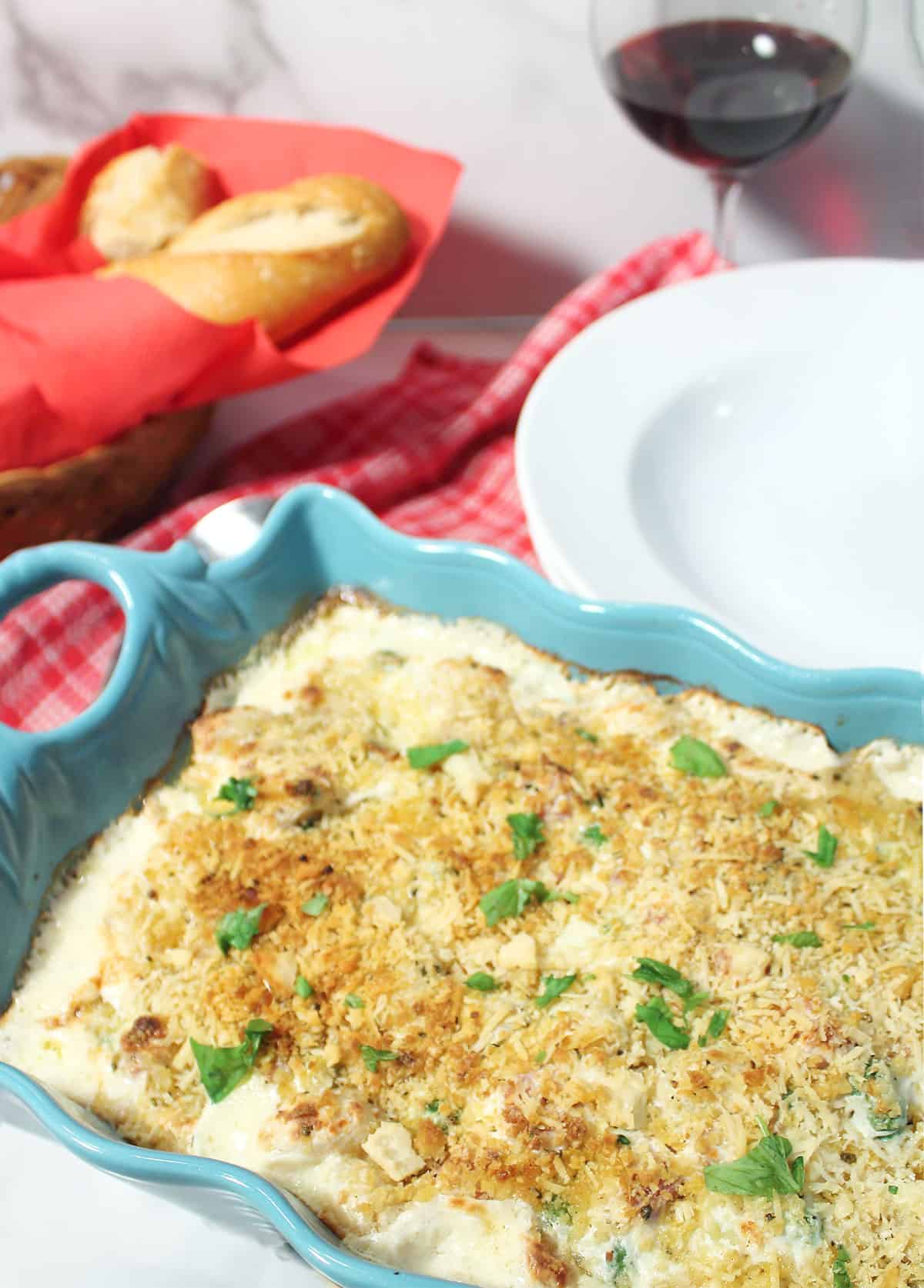 Baked gnocchi gratin casserole on dinner table with bread and wine.