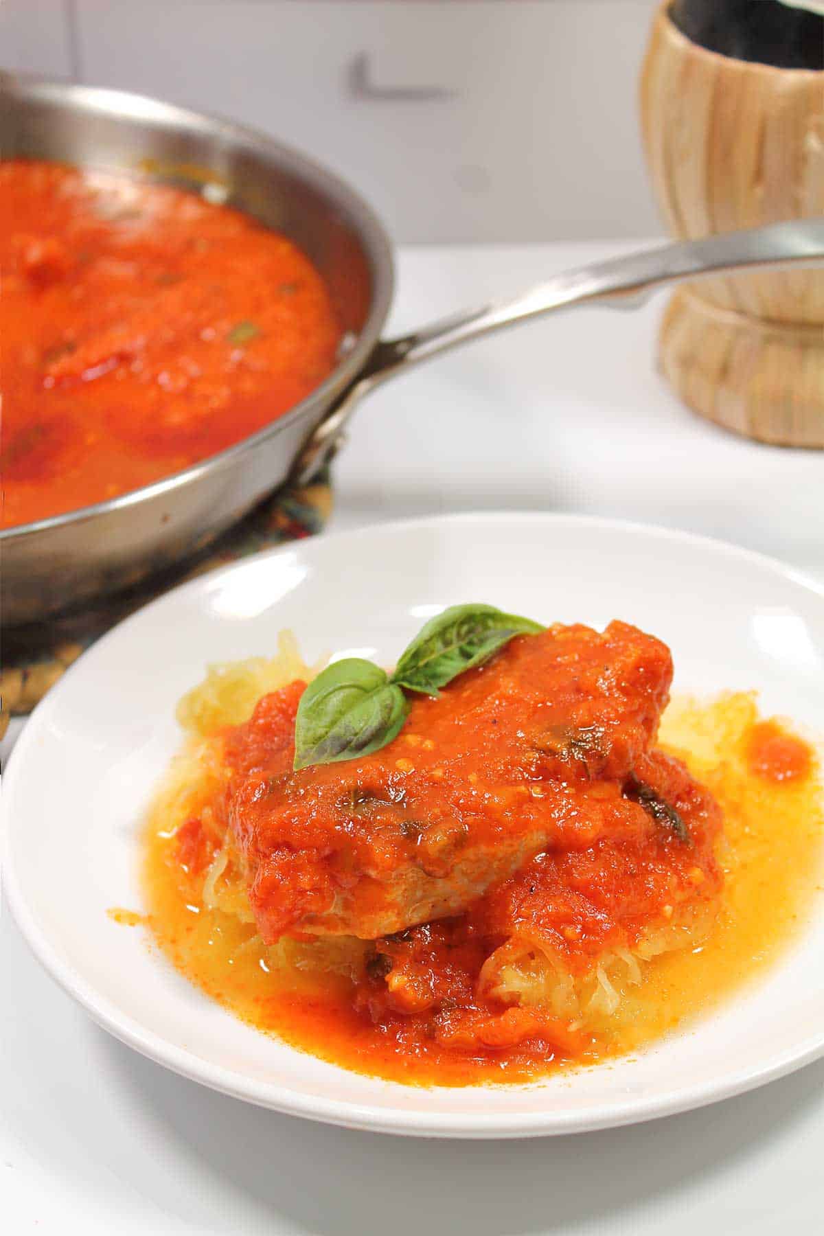 Closeup of cooked pork chop in spaghetti sauce over spaghetti squash.