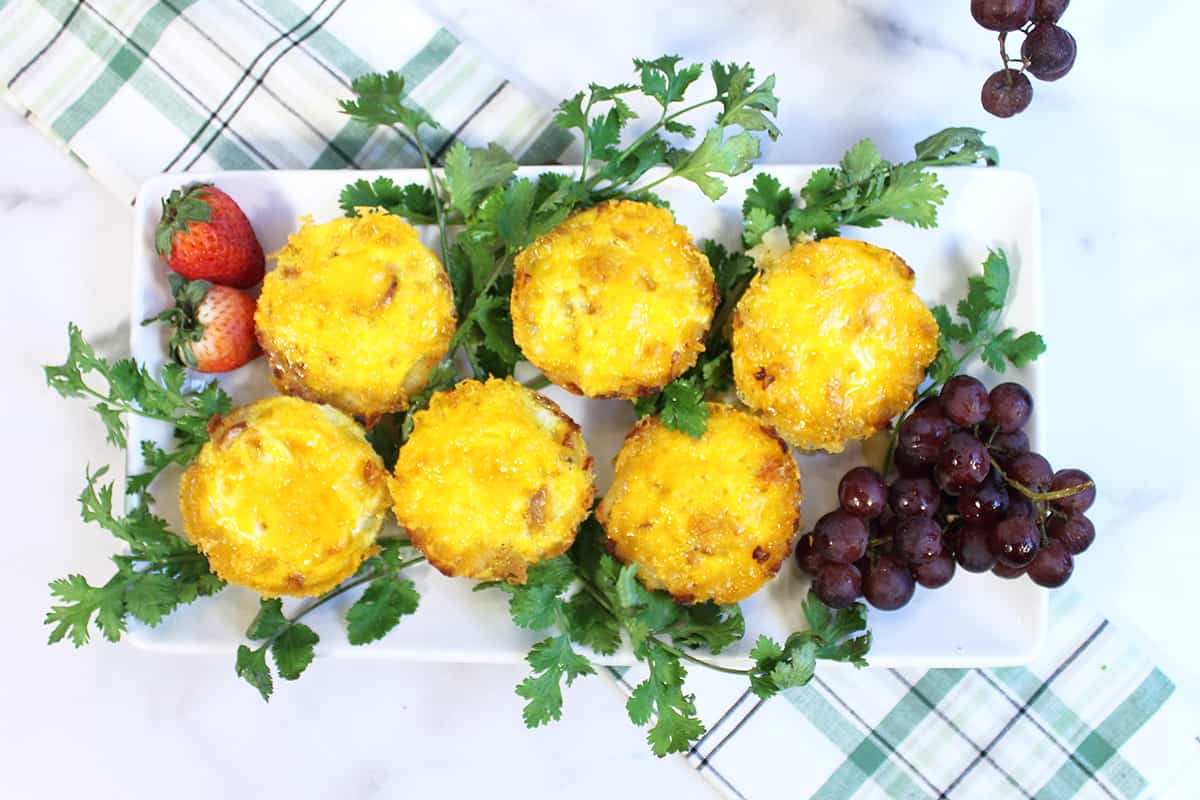 Overhead of hash brown cups with eggs on white platter with parsley and grapes.