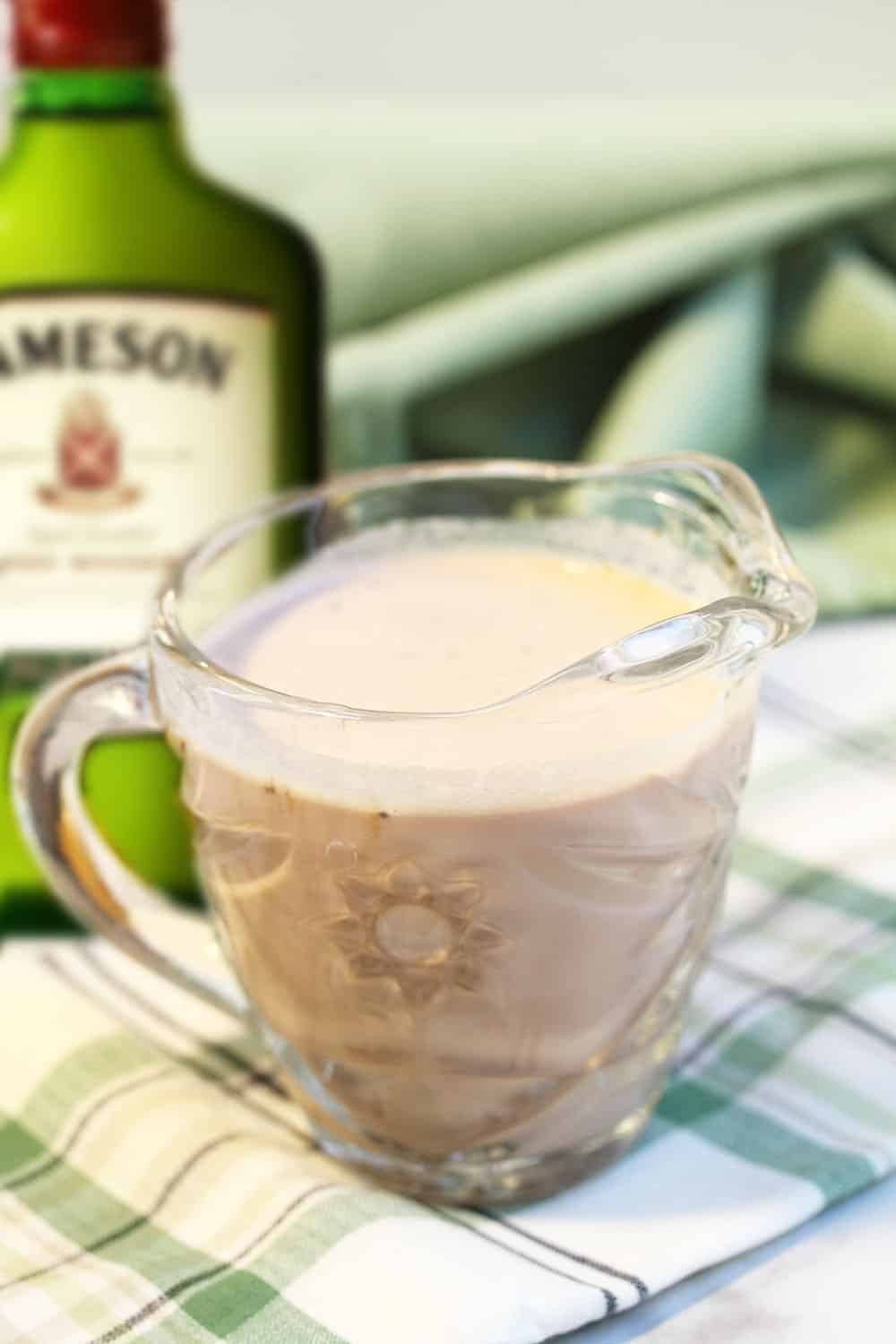 finished irish cream in glass pitcher with Jameson bottle in background.