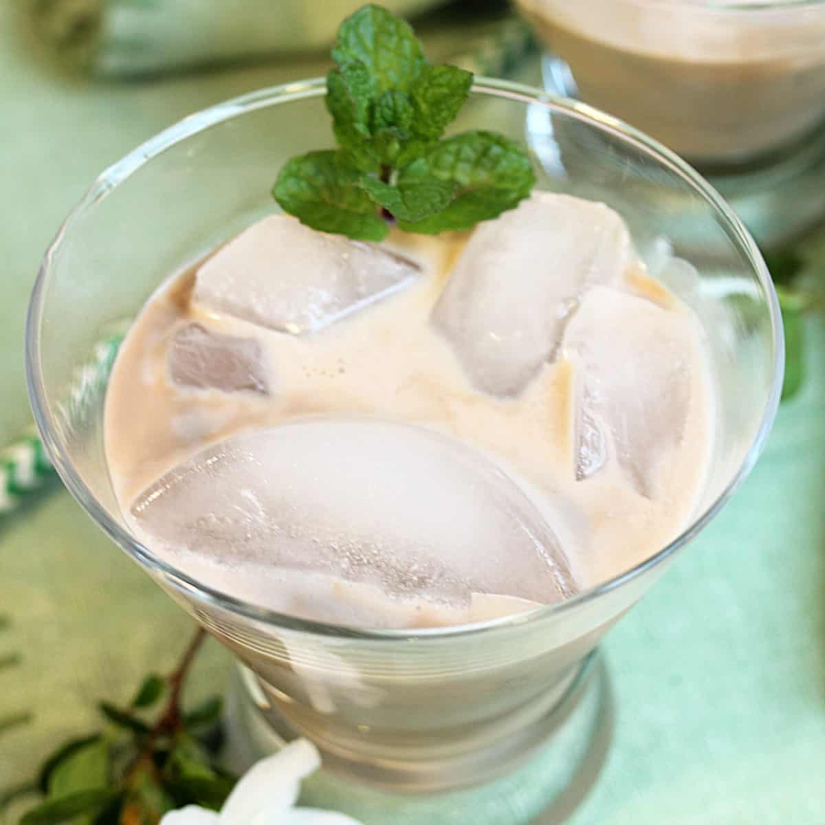 Overhead of irish cream on the rocks with sprig of mint on green napkin.