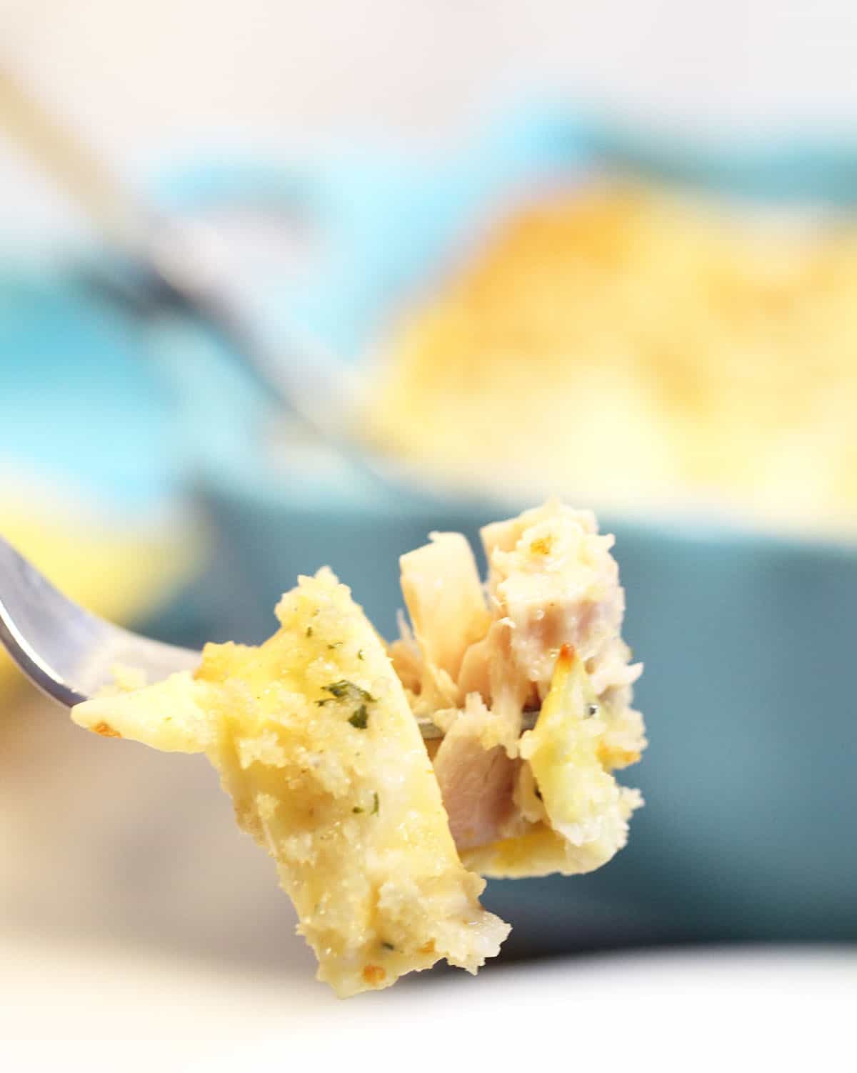 Bite of tuna and noodles on fork with turquoise casserole dish in back.