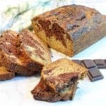 Halved piece of banana bread in front of sliced loaf with chocolate on side.