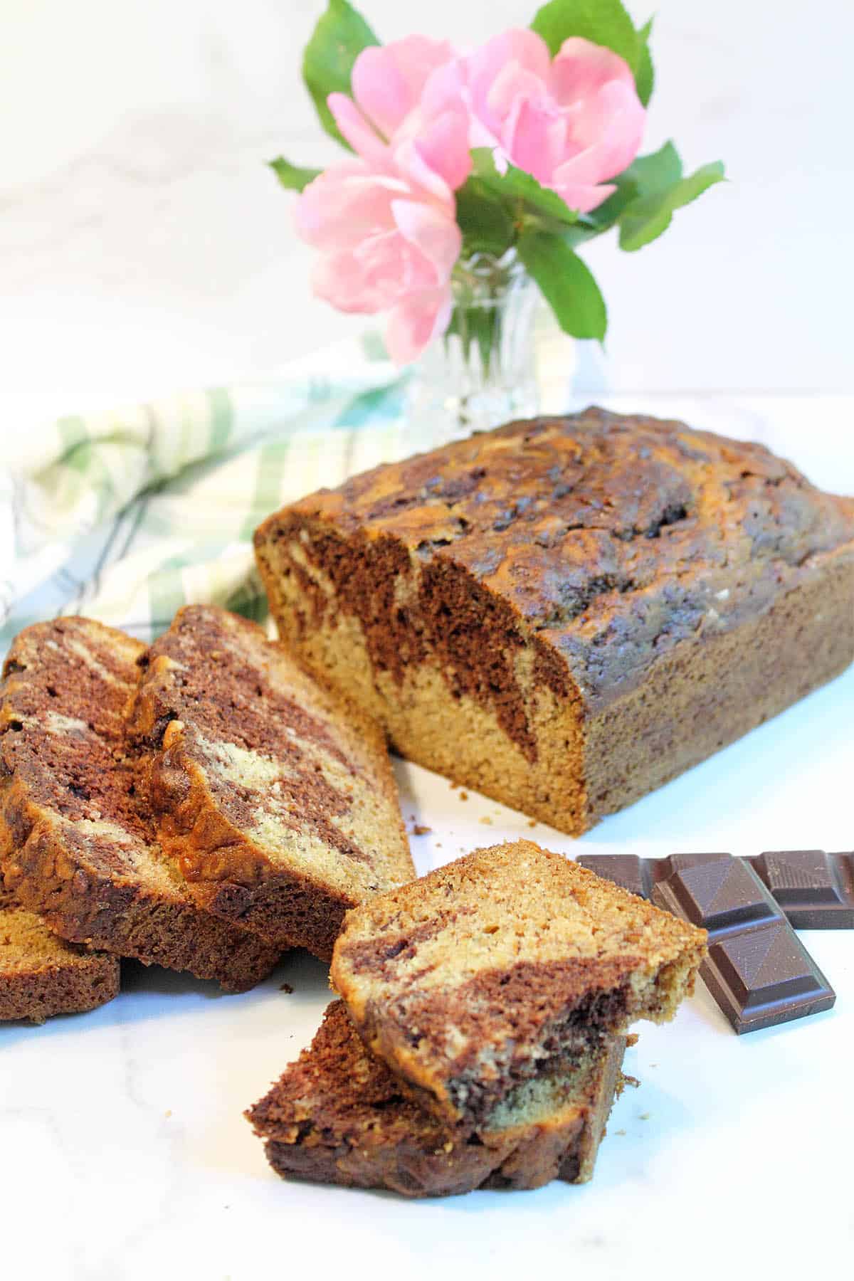 Halved piece of banana bread in front of sliced loaf with chocolate on side.