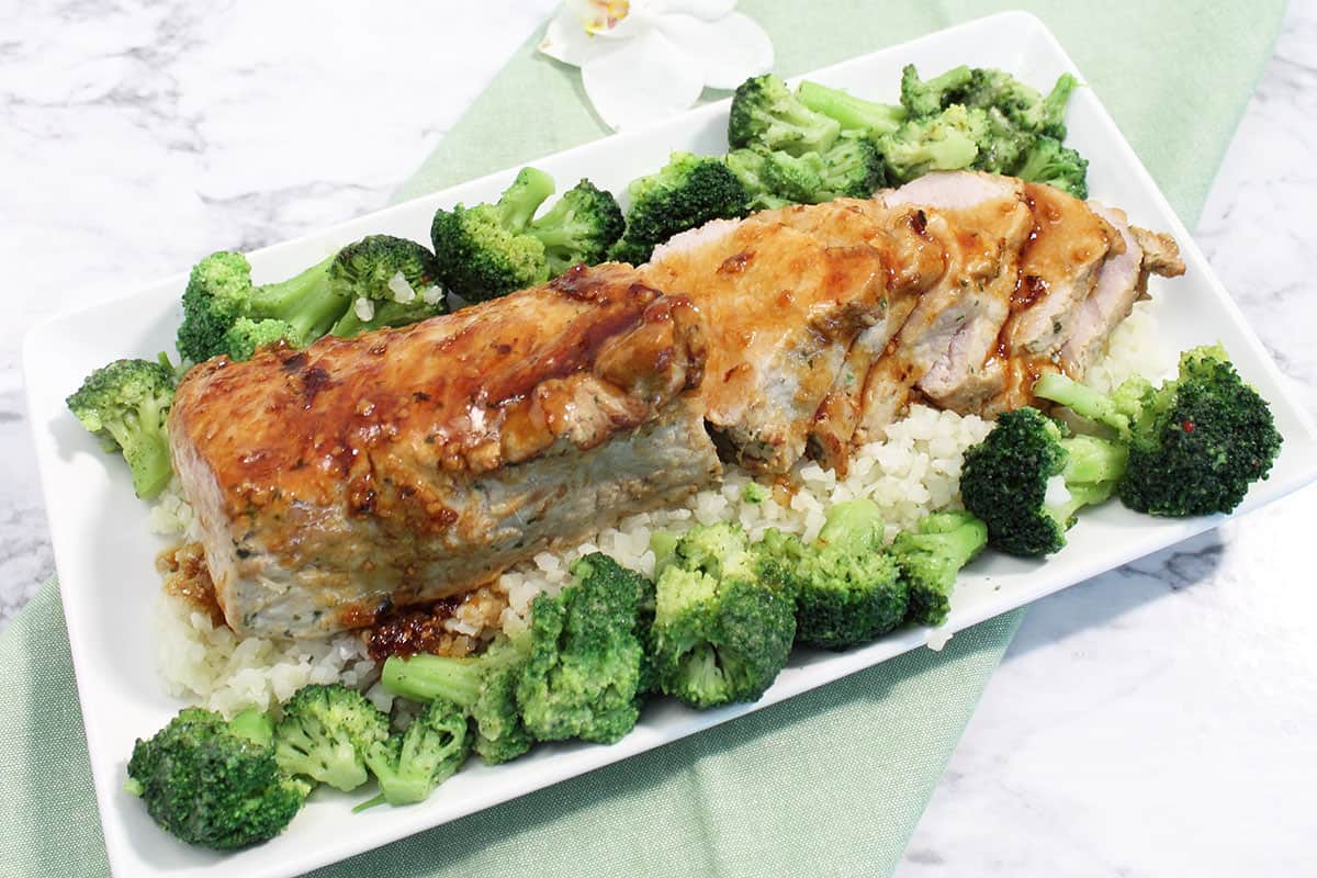 Overhead of pork loin on white serving plate with broccoli.