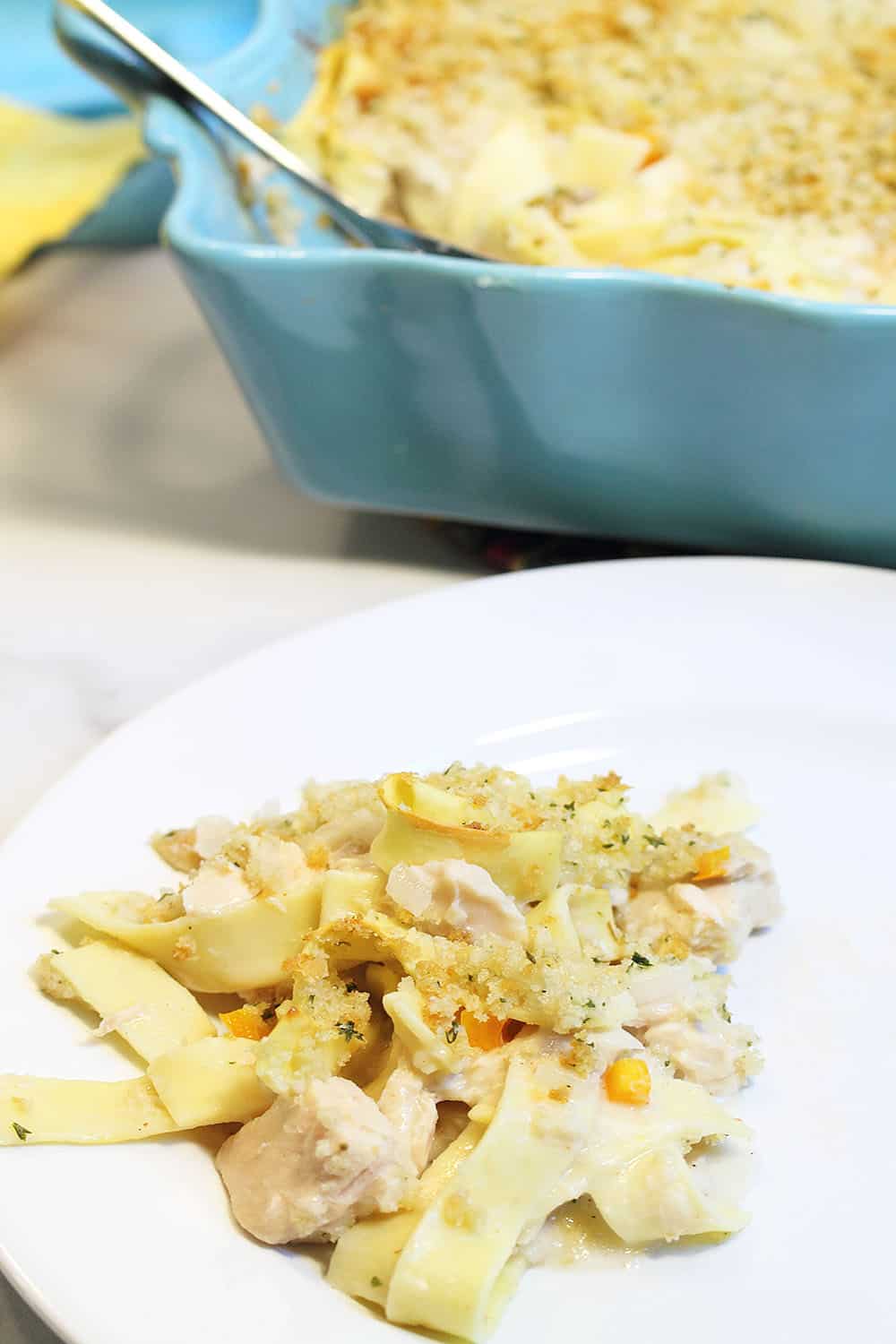 Serving of casserole on white plate with turquoise casserole dish in background.