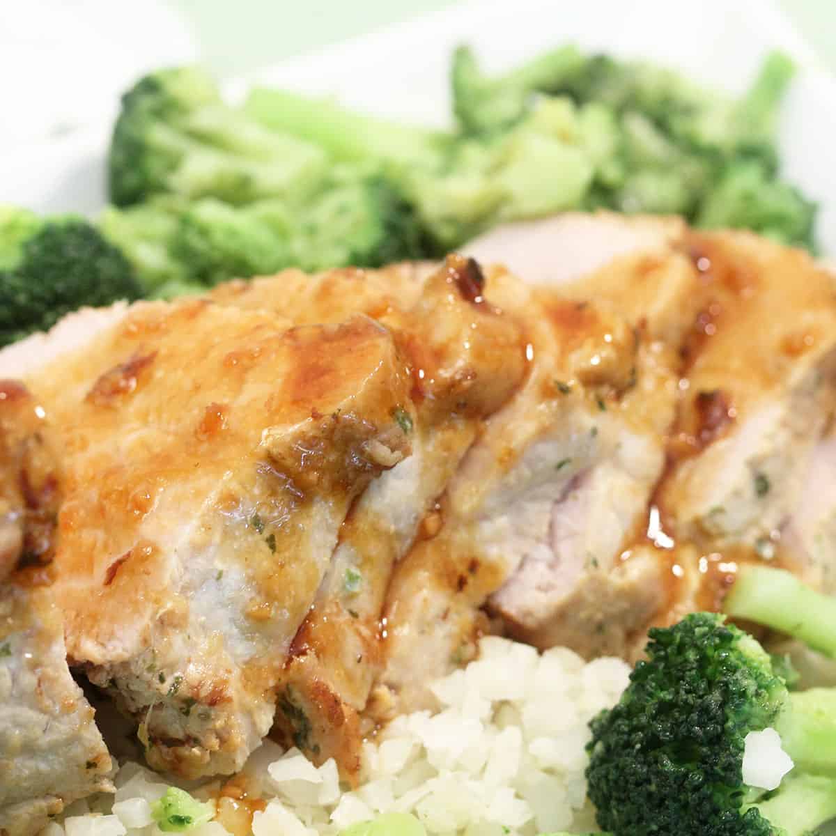Sliced pork tenderloin on white serving plate with gravy.